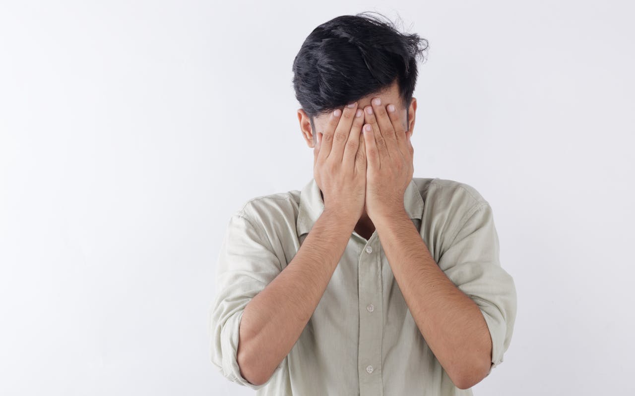 A man covering his face with hands, expressing feelings of stress and emotional struggle.